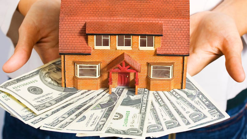 A person holding a miniature house and some dollar bills for making payments.